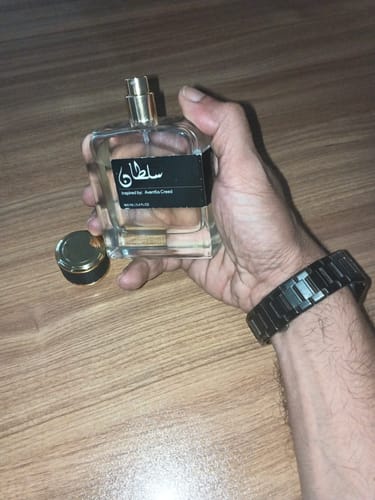 Customer's hand holding a transparent bottle of Sultan perfume, next to the small gold and black cap.