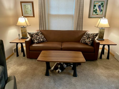 Reviewer's walnut coffee table and two end tables with black metal Nura legs in a living room with a brown sofa.
