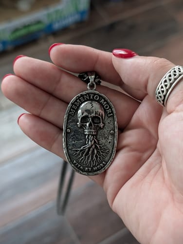 Reviewer's hand holding the antique silver Memento Mori necklace pendant, showing the skull and tree design.
