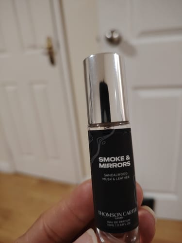 Customer's hand holding a Smoke & Mirrors Eau de Parfum sample vial, showing the clear glass and dark label.