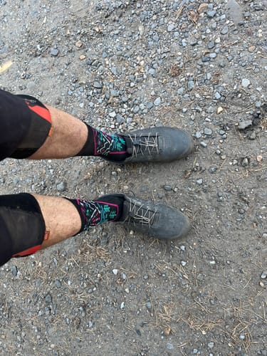 Customer's Invasion Compression Shred Socks worn with grey shoes on a rocky path.