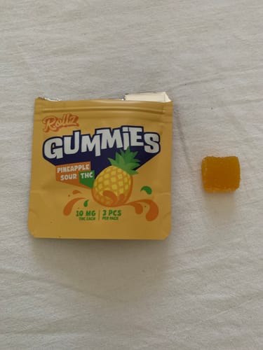Customer's ROLLZ THC pineapple sour gummy pouch next to one yellow square gummy bear.