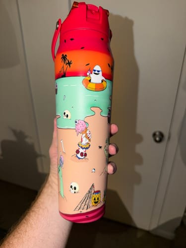 Customer's colorful Bottle Buddy 32oz Sunscream featuring cartoon beach prints being held in a hand.