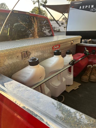 Customer's Tuff Jug 5 Gallon Jugs stored in the back of a red pickup truck next to a storage box.