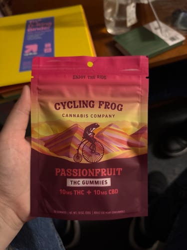 Customer's hand holding a colorful Cycling Frog Passionfruit THC gummy pouch.