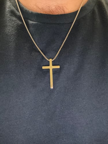 Customer's Devotion Cross, a simple silver-colored cross pendant on a matching chain worn against a dark shirt.