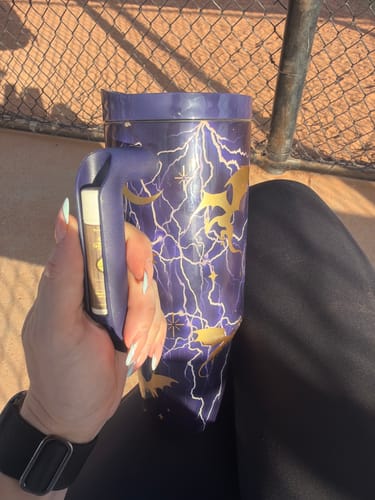 Customer's purple Thicc Buddy mug with gold dragon and lightning pattern being held at an outdoor ball field.