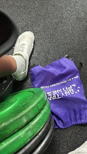 Customer's white Free I barefoot shoes worn in the gym next to gym equipment and a purple gym bag.
