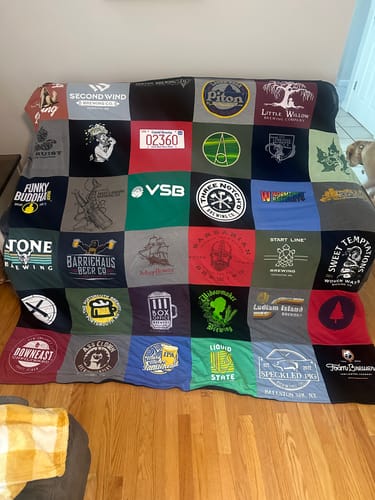 Customer's Project Repat T-Shirt Quilt featuring various brewery logos on multi-colored fabric squares, displayed on a chair.