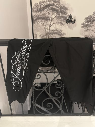 Customer's black JR Signature cargo-style baggy pants with white cursive embroidery hanging on a metal railing.