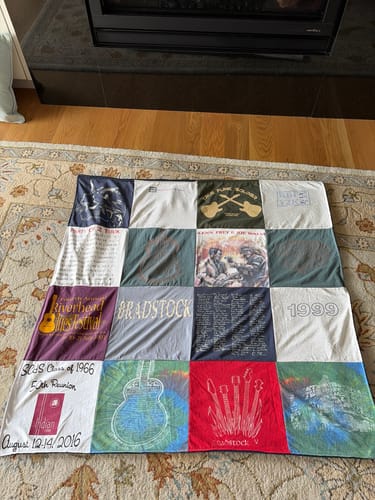 Customer's Project Repat T-Shirt Quilt featuring various graphic tee squares laid flat on a patterned rug.