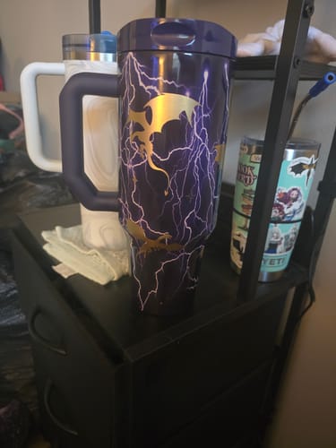 Customer's purple Thicc Buddy tumbler with lightning and dragon designs sitting on a black shelving unit