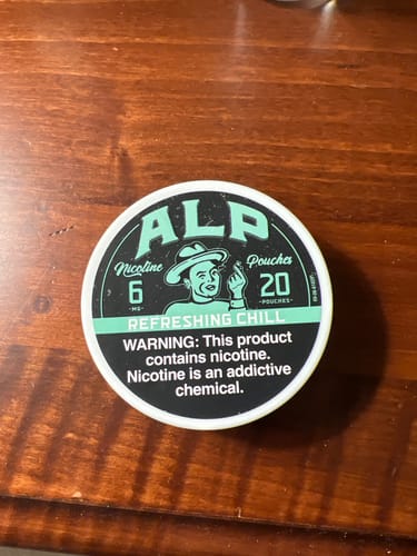 Customer's round ALP Refreshing Chill nicotine pouch tin, set on a brown wooden surface.
