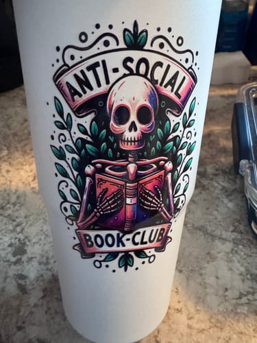 Customer's white To-Go Buddy tumbler featuring a colorful illustration of a skeleton reading a book.