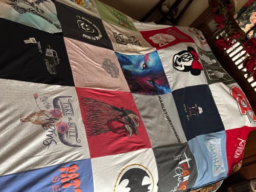 Customer's Project Repat T-Shirt Quilt spread on a bed, showing various colorful, patterned t-shirt panels.