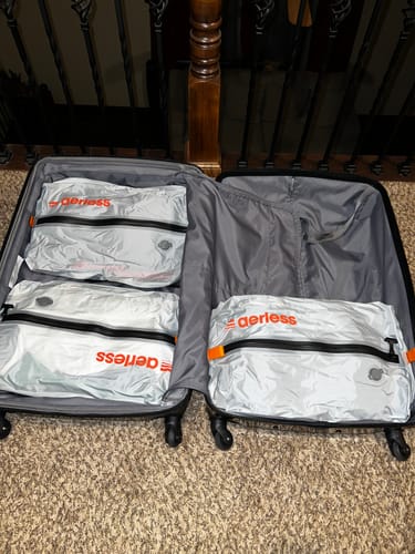 Customer's open suitcase packed with three silver Aerless vacuum bags featuring black zippers and orange branding.