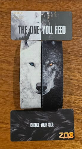 Customer's The One You Feed Light Wolf Bracelet, showing white and black wolf designs with cards on a wooden surface.