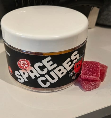 Kundenfoto der THC Space Cubes Dose mit drei roten, zuckerbestreuten Fruchtgummis auf einer weißen Oberfläche.