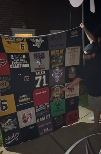 Reviewer showing a completed Premium T Shirt Quilt, pointing to a sports square with balanced t-shirt designs.