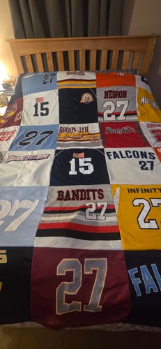 Customer's Project Repat T-Shirt Quilt featuring numerous sports jerseys with numbers like 15 and 27 laid on a bed.