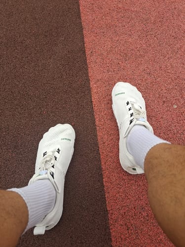 Customer's white Free I barefoot shoes worn on feet while standing on an outdoor track.