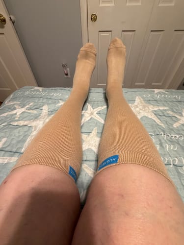 Customer's Eucalyptus Lyocell Compression Socks on legs, worn with the top band folded over while resting on a bed.