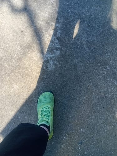Reviewer's lime green Smart I Pro barefoot shoe on a concrete path, capturing the wide toe box design.