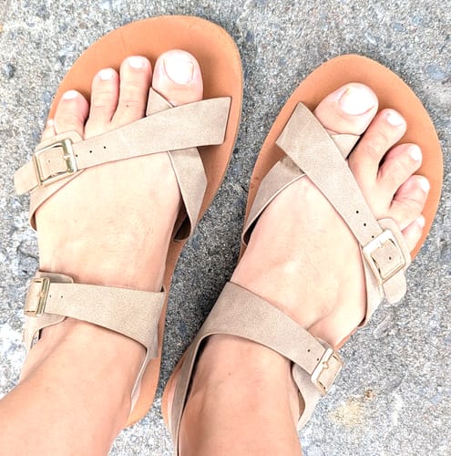 Customer's feet wearing tan Glow II Barefoot Sandals with supportive back straps on a gray concrete surface.
