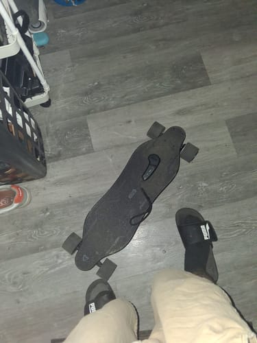 Reviewer's black refurbished skateboard resting on a gray floor, seen from a top-down view.