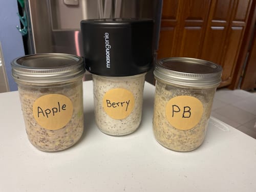 Reviewer's black Mason Genie sealing device placed on one of three mason jars filled with oats and chia seeds.