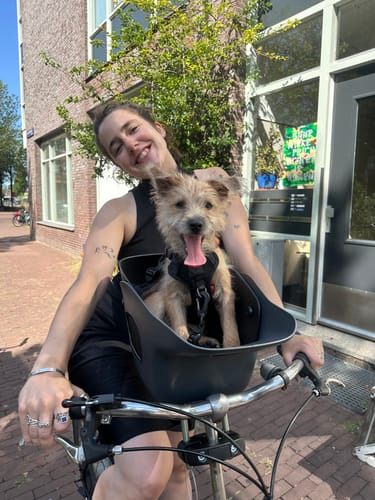 Reviewer smiling with a small dog in a dark Kvisp Dog Bike Carrier attached to their bike handle.