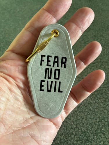 Customer's hand holding a gray Fear No Evil Bible Verse keychain with a gold carabiner.