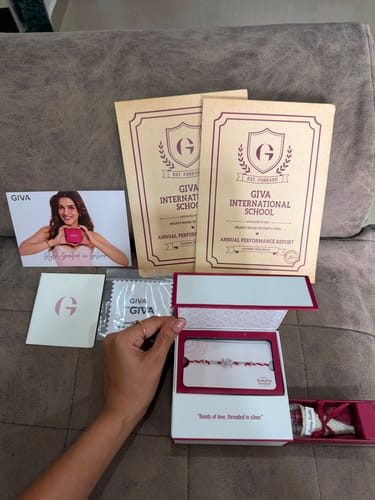 Customer's Silver Symbolic Swastik Rakhi in open white presentation box, displayed with GIVA card and documents