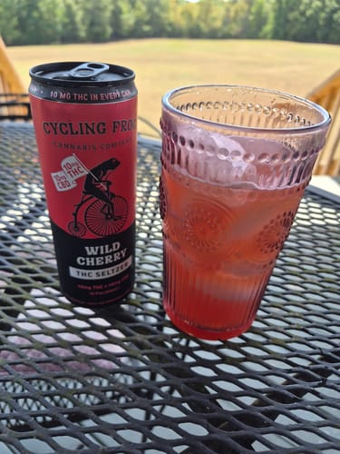 Customer's Wild Cherry THC Seltzer can and a glass of red bubbly seltzer sitting on a table outdoors.