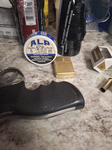 Reviewer's ALP Chilled Mint nicotine pouch container next to a gold lighter and other items on a counter