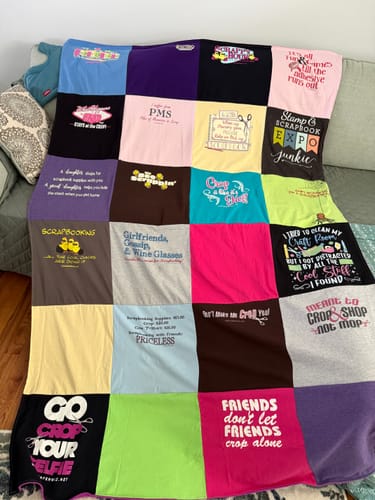 Customer's Project Repat T-Shirt Quilt displayed on a couch, featuring a grid of colorful shirts with scrapbook themes.