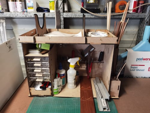 Customer's Mueble taller organizador de madera montado sobre una mesa, lleno de herramientas y materiales de modelismo.
