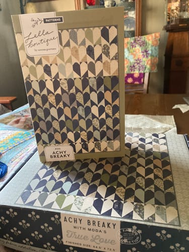Reviewer's Achy Breaky Pre-Cut Quilt Kit box with quilt pattern and fabric collection displayed on a table