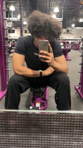 Customer's black Batman compression tee worn while sitting on a gym bench, reflecting in a mirror.