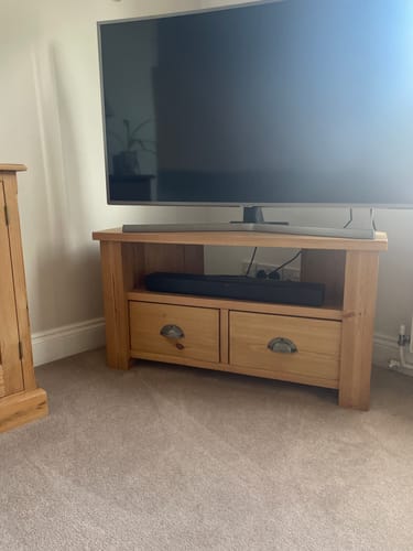 Customer's Wooden Corner TV Stand in a living room, featuring a television on top, a soundbar, and two drawers.