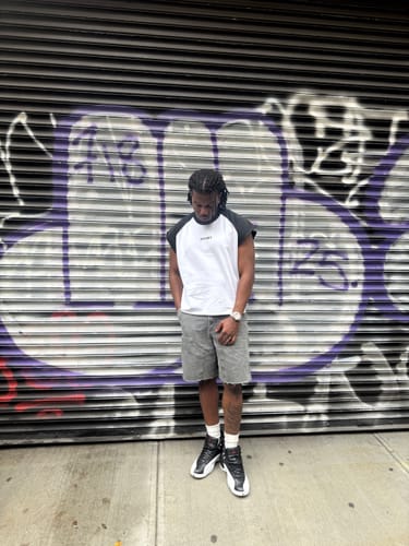 Customer's Raw Raglan Tank, worn by a person standing against a graffiti-covered rolling gate.