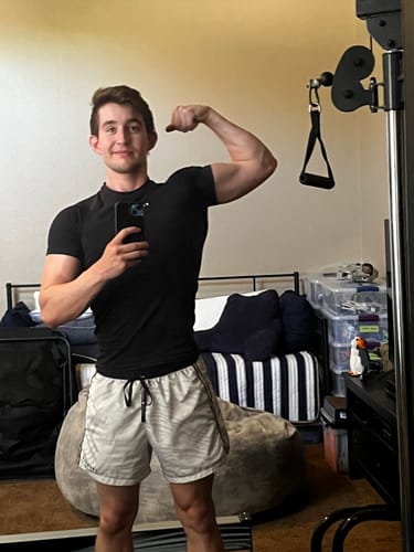 Customer's black SuperVillain compression tee worn while flexing arm in a bedroom.