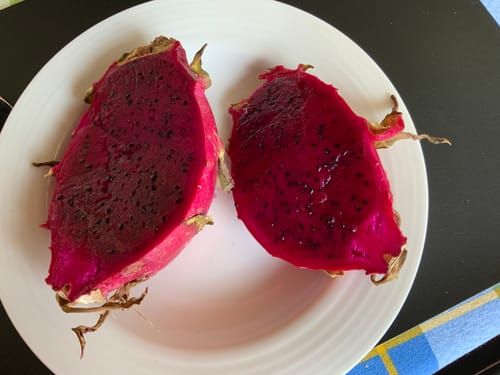Kundenfoto einer halbierten, leuchtend roten Drachenfrucht von Julian auf einem weißen Teller.