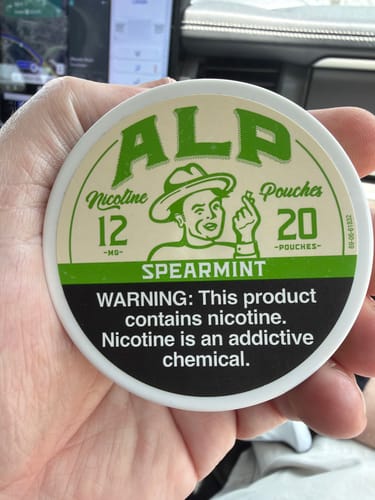 Customer's hand holding a round, green and white ALP Spearmint nicotine pouch container.