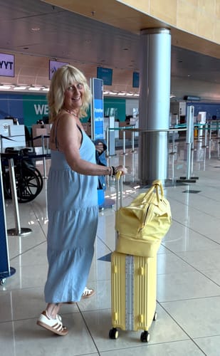 Reviewer's butter yellow Weekender Bag stacked on a matching carry-on suitcase at an airport terminal.