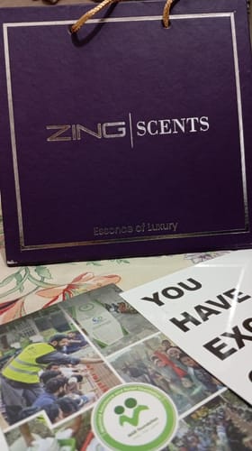 Customer's purple Zing Scents shopping bag placed on a surface with a printed card containing collage images.