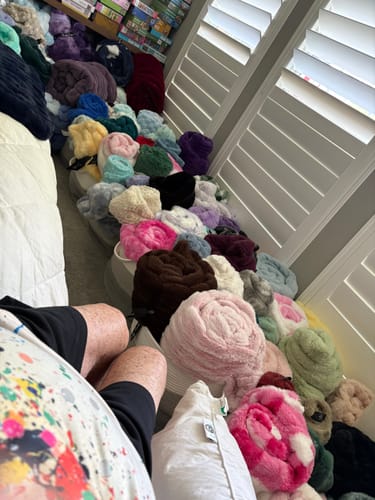 Reviewer's collection of many soft, plush Hugs Lizi blankets in various colors piled in baskets near a window.