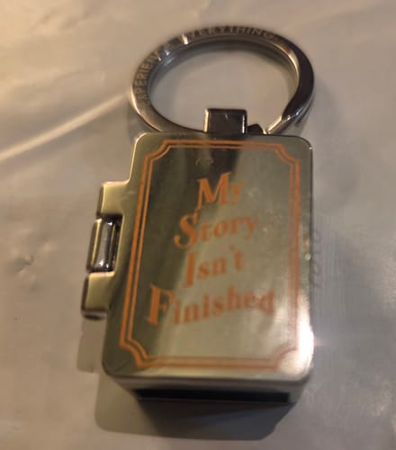 Customer's My Story Isn't Finished Zoxlox keychain, silver metal locket with text engraved on the front.