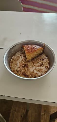 Customer's Traditional Greek Portokalopita, a golden brown orange syrup cake, remaining in a round metal baking pan.