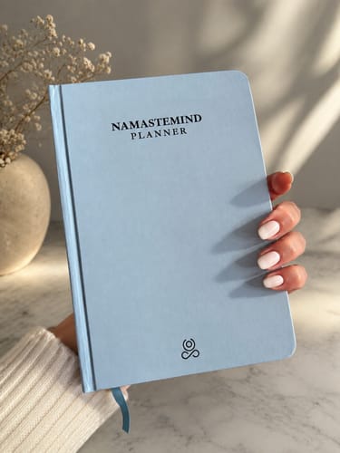 Customer's hand holding a light blue Namastemind planner against a bright, minimalist background.